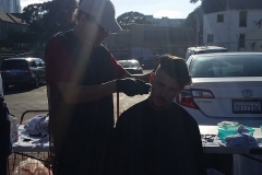 The light shines down on the stylist while giving hair cuts to a homeless man.